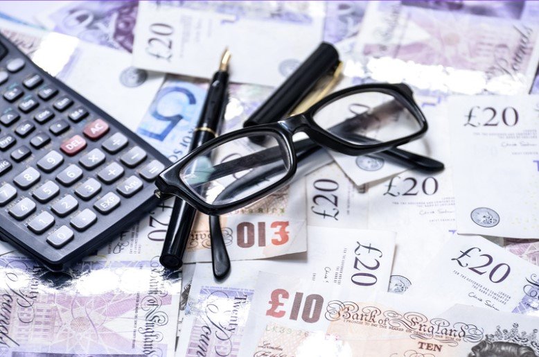 Close-up of British pound sterling banknotes, a calculator, and spectacles.